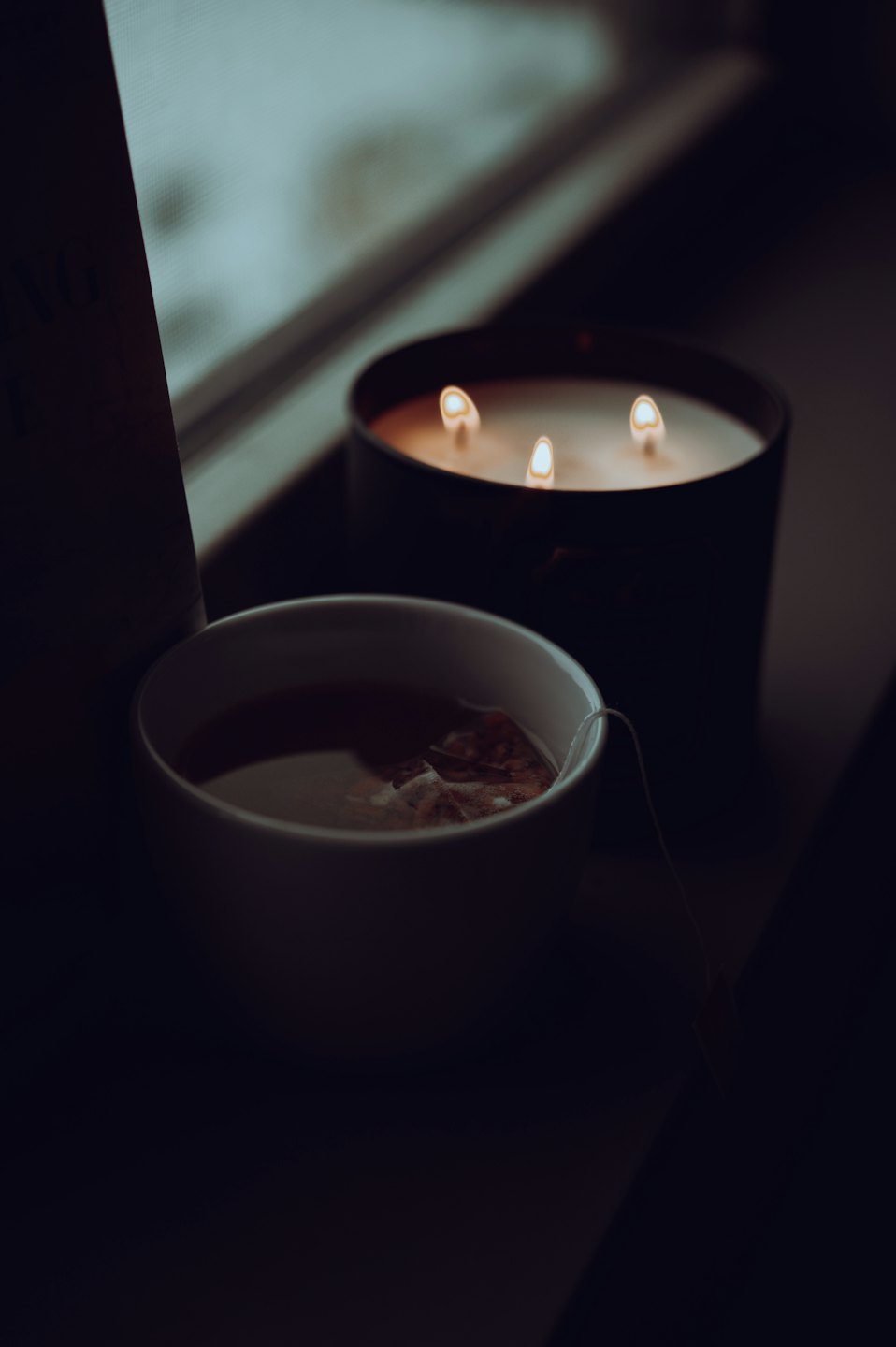 A steaming teacup rests beside a lit three-wick candle.