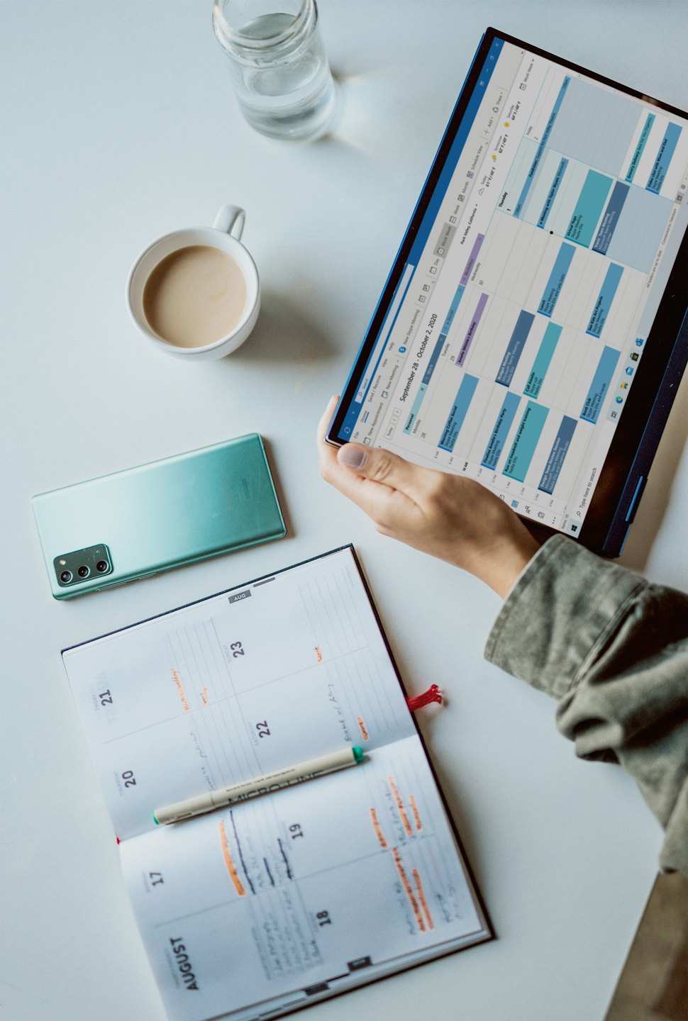 Hands planning on a tablet and planner with coffee.