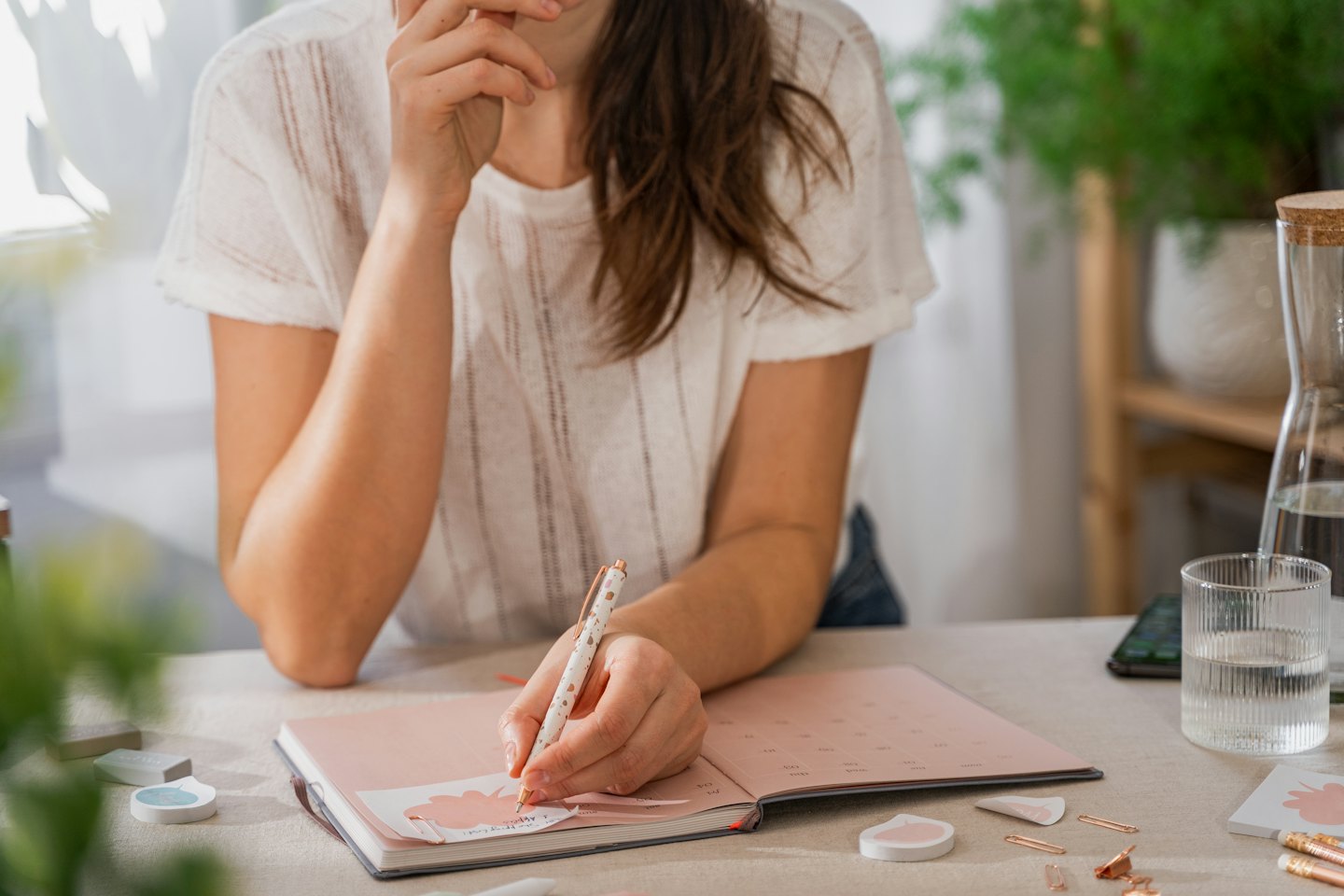 Woman writes in a pink planner at a desk with office supplies.
